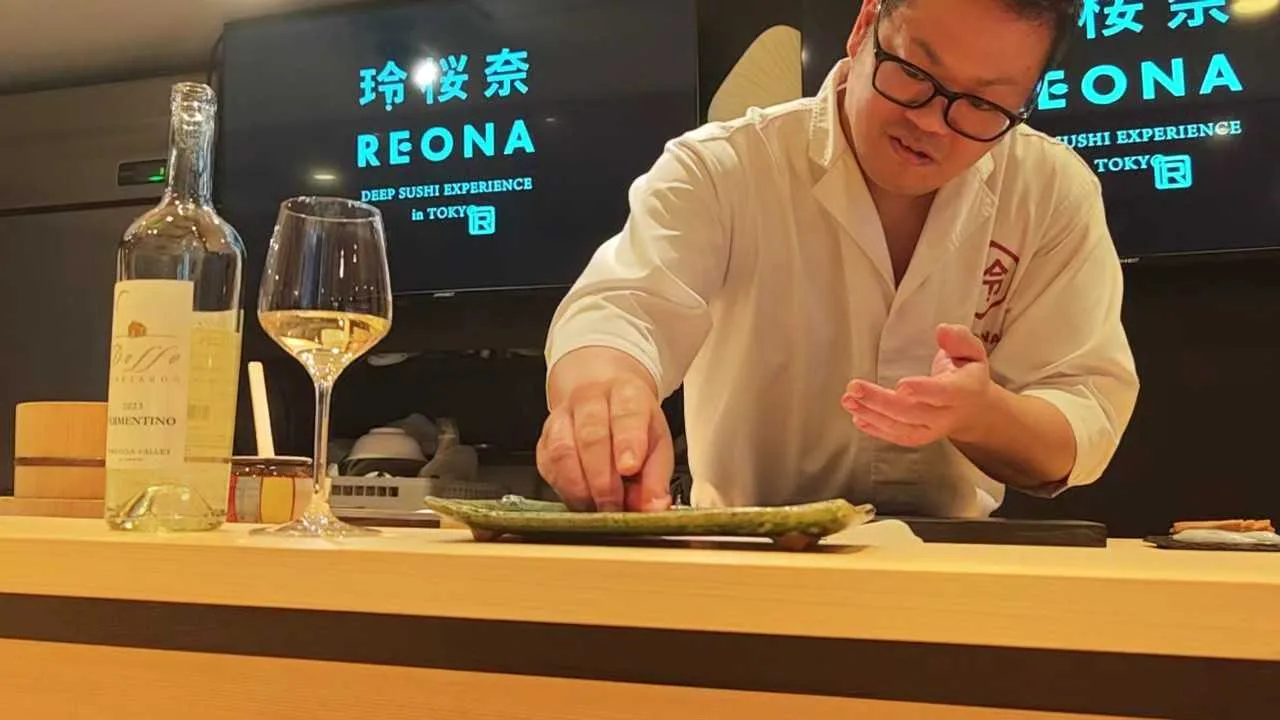 The chef serving sushi with a glass of white wine at the REONA counter