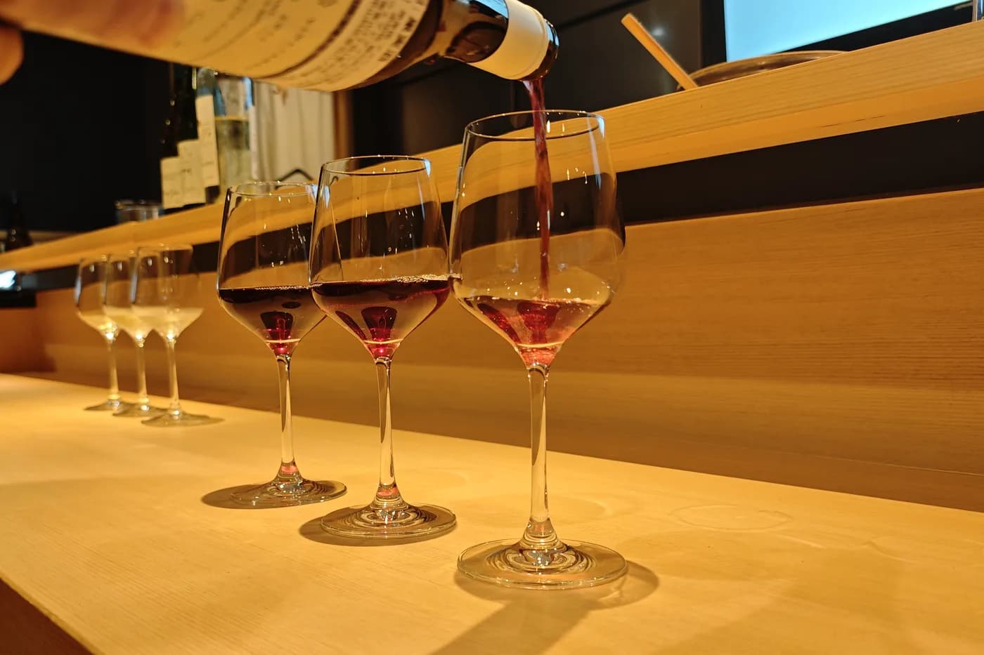 Red wine being poured into a line of glasses at the REONA counter