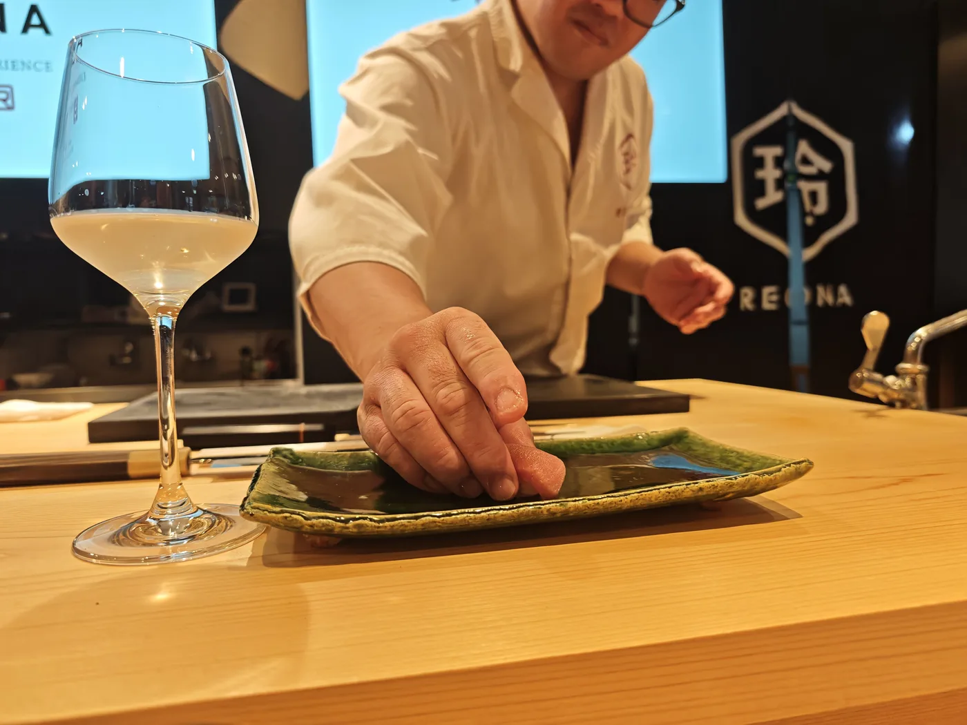A piece of sushi served on a plate beside a glass of white wine